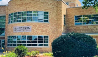 Image of the mottled tan brick and glass Atchison Event Center with the name sign in the middle and bushes in front.